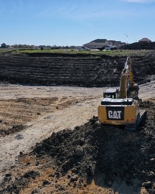 CAT excavator grading a residential home pad with houses visible in the background